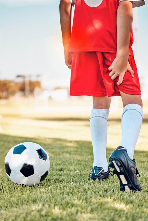 boy holding his hamstring with a soccer ball on the grass