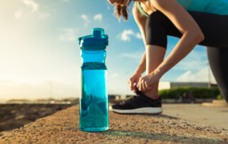 blue water bottle next to woman tying her sneaker lace