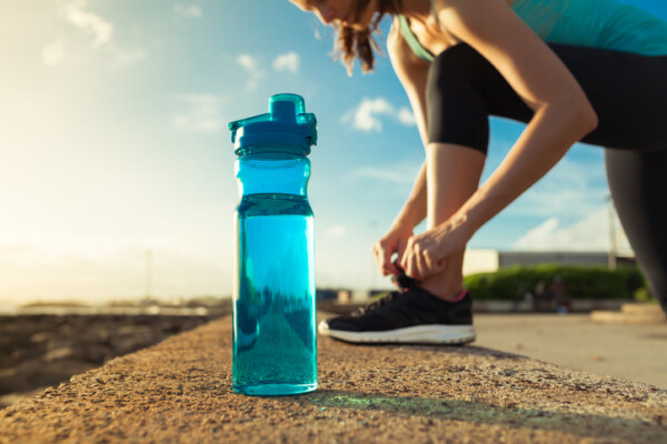 blue water bottle next to woman tying her sneaker lace