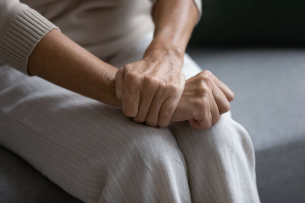 Close up of elderly woman sit on sofa with hands clenched