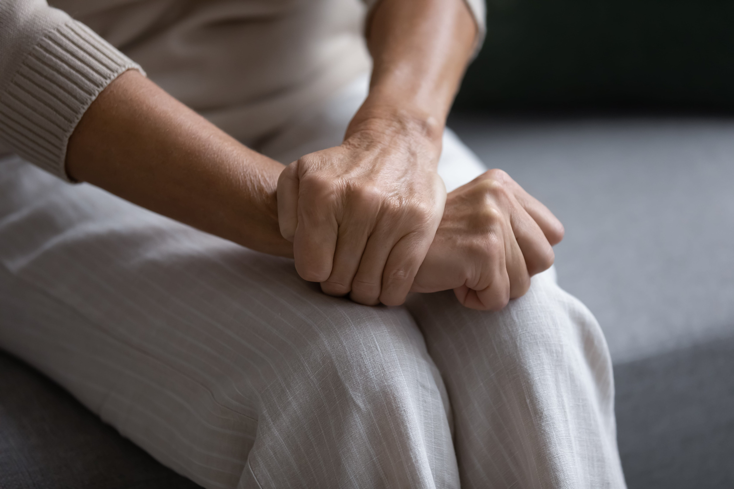 Close up of elderly woman sit on sofa with hands clenched